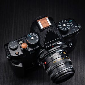 以下が含まれることがあります： 木製のシャッターボタンと木製のホットシューカバーを備えた黒いNikon Zfミラーレスカメラ。カメラにはSHOTEN L.M-N.Z IIと刻印された黒いレンズが装着されており、白と黄色の絞り値と距離の目盛りが表示されています。
