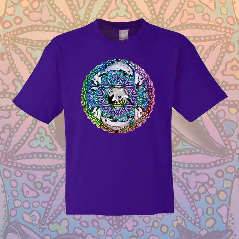May include: A purple t-shirt featuring a colorful mandala design with dolphins. The mandala is a vibrant mix of blues, greens, and pinks, with white dolphins arranged around a central geometric pattern. The shirt is a classic crew neck style.