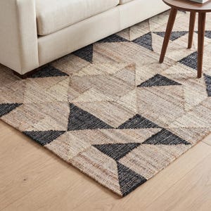 May include: A woven area rug featuring a geometric pattern of triangles in natural tan and dark charcoal gray. The rug has a textured, fibrous appearance with a repeating design of alternating light and dark triangular shapes across the surface.