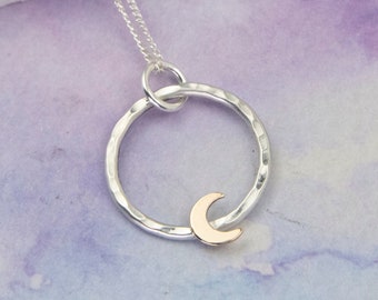May include: A silver necklace with a hammered circle pendant and a small gold crescent moon charm.