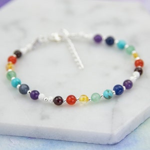 Peut inclure: Un bracelet en argent avec des perles de pierres précieuses colorées. Les perles sont disposées en arc-en-ciel, chaque couleur représentant un chakra différent.