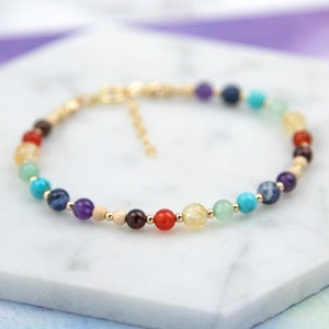 Peut inclure: Un bracelet en or avec des perles de pierres précieuses de différentes couleurs. Les perles sont disposées en arc-en-ciel, du rouge au violet.