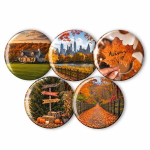 May include: A set of five circular magnets featuring autumn-themed imagery: a house with orange trees, a city skyline, a hand holding a leaf with the word Autumn written on it, a signpost pointing to corn maze, pumpkins, and hayrides, and a leaf-covered path.
