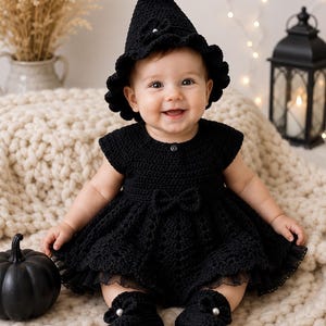 Puede incluir: Un vestido negro de ganchillo con un sombrero puntiagudo y patucos a juego. El vestido presenta un corpiño de manga corta, una falda acampanada con un pequeño lazo en la cintura y un dobladillo con volantes. El sombrero tiene una flor y una cuenta.