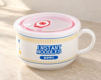 May include: A white ceramic bowl with a handle, featuring a translucent lid with a red vent. The bowl has yellow striped borders and blue text that reads INSTANT NOODLES BOWL, along with a small yellow smiley face icon on the side.