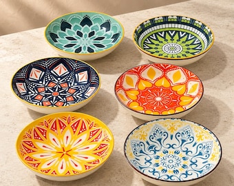 May include: A set of six round ceramic bowls, each featuring a unique, vibrant, multi-colored geometric pattern. The designs include floral-inspired motifs in shades of teal, lime green, navy blue, orange, yellow, and white.