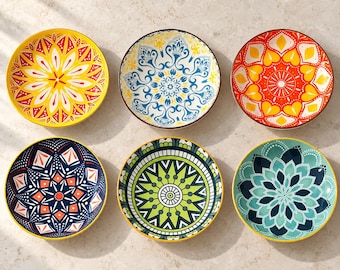 May include: A set of six round ceramic bowls arranged in two rows of three. Each bowl features a distinct, colorful, and symmetrical geometric pattern in shades of yellow, red, blue, green, and teal, with intricate radial designs.