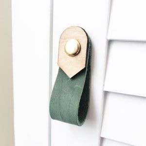 Puede incluir: Un tirador de armario de cuero verde con una parte superior de madera y un pomo dorado.