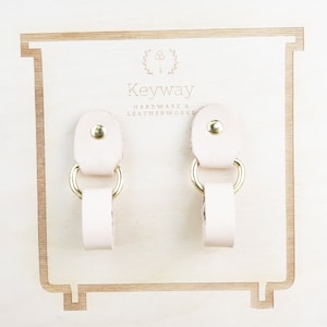 May include: Two light pink leather straps with gold metal rings. The straps are attached to a wooden board with the text "Keyway Hardware & Leatherworks".