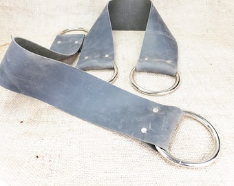 May include: Two gray leather straps with silver metal rings. The straps are thick and have a worn look. The rings are large and round.