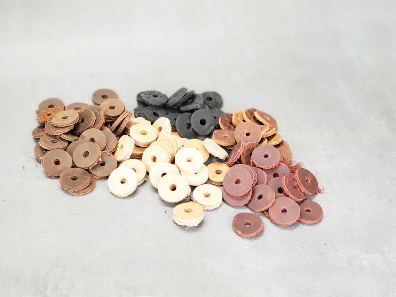 May include: Assortment of leather rings in brown, tan, black, and burgundy colors. The rings are stacked in a pile on a gray surface.