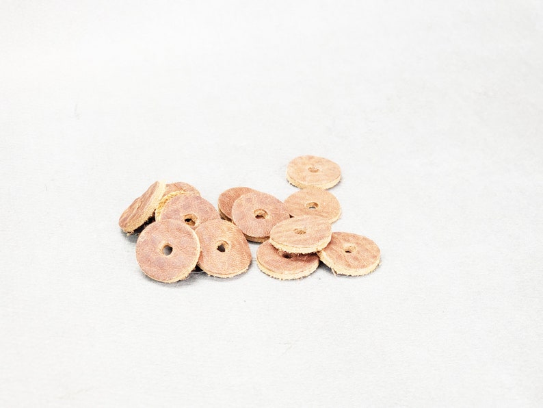 May include: A pile of brown leather round discs with a hole in the center. The discs are arranged in a random pattern on a white surface.