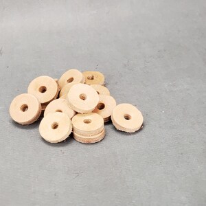 May include: A pile of light brown leather washers. The washers are round with a hole in the center. They are arranged in a random pattern.