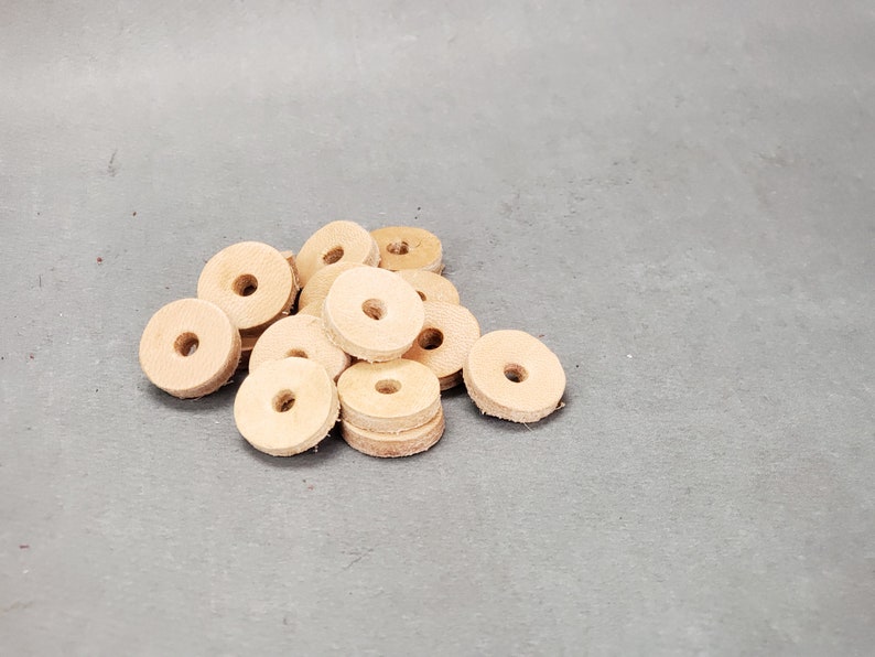 May include: A pile of light brown leather washers. The washers are round with a hole in the center. They are arranged in a random pattern.