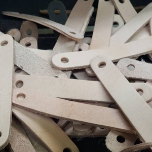May include: A pile of light brown leather straps with holes punched at each end. The straps are all different lengths and widths.
