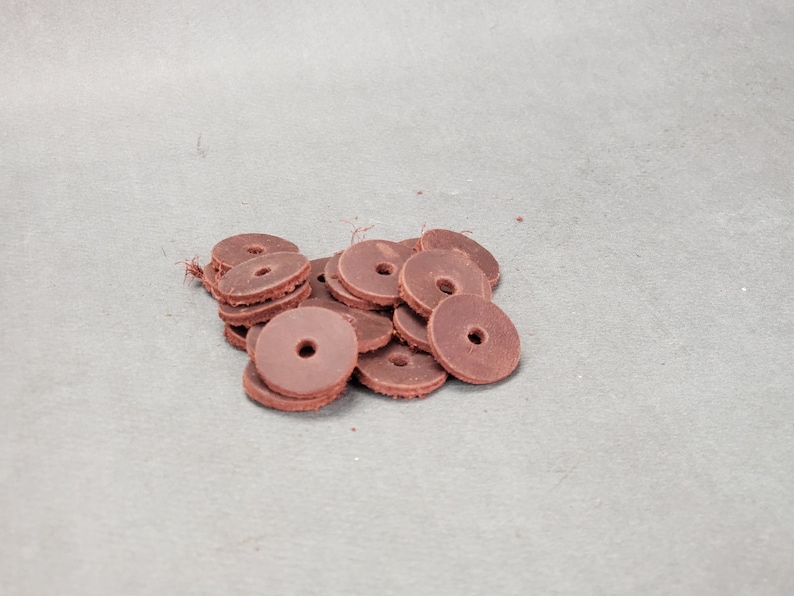 May include: A pile of brown leather washers, stacked and overlapping. The washers are round with a hole in the center.