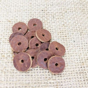 May include: A pile of brown leather rings with a hole in the center. The rings are on a burlap background.