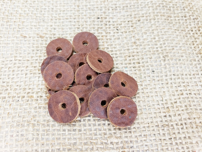 May include: A pile of brown leather rings with a hole in the center. The rings are on a burlap background.
