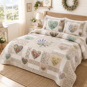 Puede incluir: Una colcha acolchada y dos fundas de almohada a juego con un diseño de patchwork de patrones florales y aplicaciones en forma de corazón. La colcha muestra varias ilustraciones botánicas en colores pastel suaves, incluyendo lavanda, rosas y flores silvestres.