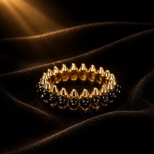 May include: A circular ring featuring a repeating pattern of alternating gold-toned metal spikes and smooth, round black beads. The design consists of a continuous band of these elements arranged in a symmetrical, spiked formation around the circumference.