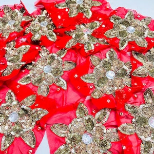 May include: A collection of red fabric patches featuring gold sequin floral embroidery and a central clear faceted stone. Each flower-shaped applique is crafted with metallic gold thread and scattered sequins on a vibrant red base material.