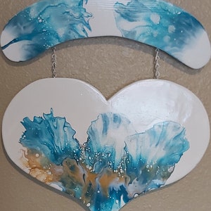 May include: A white heart-shaped wooden sign with a blue and white abstract design. The heart is hanging from a white wooden arch with a similar blue and white abstract design.