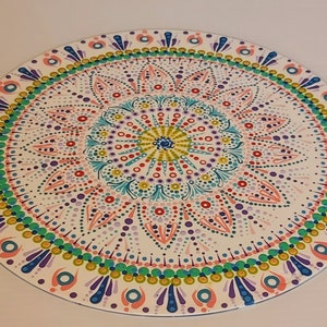 May include: A colorful mandala design painted on a round wooden surface. The mandala features a variety of colors, including pink, blue, green, yellow, and white. The design is intricate and detailed, with a central circle surrounded by concentric rings of dots and patterns.