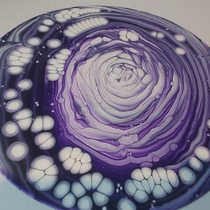 May include: A circular painting with a swirling purple and white design. The center of the painting is a spiral of purple and white, surrounded by a ring of white dots.