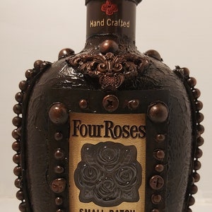 May include: A brown glass bottle with a decorative stopper and a label that reads "Four Roses Small Batch Kentucky Straight Bourbon Whiskey Crafted from Four Select Bourbons 45% ALC./VOL. (90 proof/ 750ML)"
