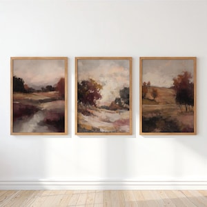 Puede incluir: Un conjunto de tres cuadros rectangulares con marcos de madera clara, cada uno con una pintura de paisaje impresionista en tonos apagados de marrón, rojo oscuro y gris suave, que representan colinas, árboles y cielos nublados.