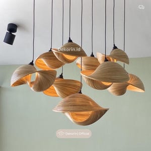 Può includere: Un gruppo di lampade a sospensione multiple con paralumi color marrone chiaro, curvi e simili al bambù, caratterizzati da un design a spirale che ricorda una conchiglia. Ogni paralume è appeso al soffitto con un sottile cavo nero.