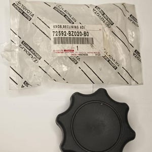 Könnte beinhalten: Ein schwarzer Sitzverstellknopf aus Kunststoff in Form eines sechsstrahligen Sterns. Er wird von einer durchsichtigen Kunststoffverpackung mit Toyota- und Lexus-Logos begleitet, die ein Etikett mit der Aufschrift KNOB RECLINING ADJ 72592-BZ020-B0 trägt.