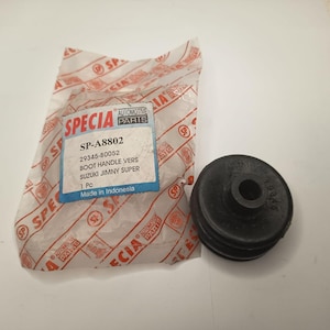 Puede incluir: Una pieza de automóvil de goma negra junto a su embalaje de plástico blanco. El embalaje presenta el texto SPECIA AUTOMOTIVE PARTS, SP-A8802, 29345-80052, BOOT HANDLE VERS SUZUKI JIMNY SUPER, 1 Pc, y Made in Indonesia en una etiqueta azul y blanca.