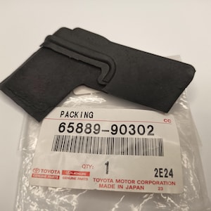 May include: A black rubber packing component with a distinct angled shape and a molded hook feature. It is positioned on a clear plastic bag featuring a white label with the text PACKING, 65889-90302, QTY 1, and Toyota and Lexus logos.