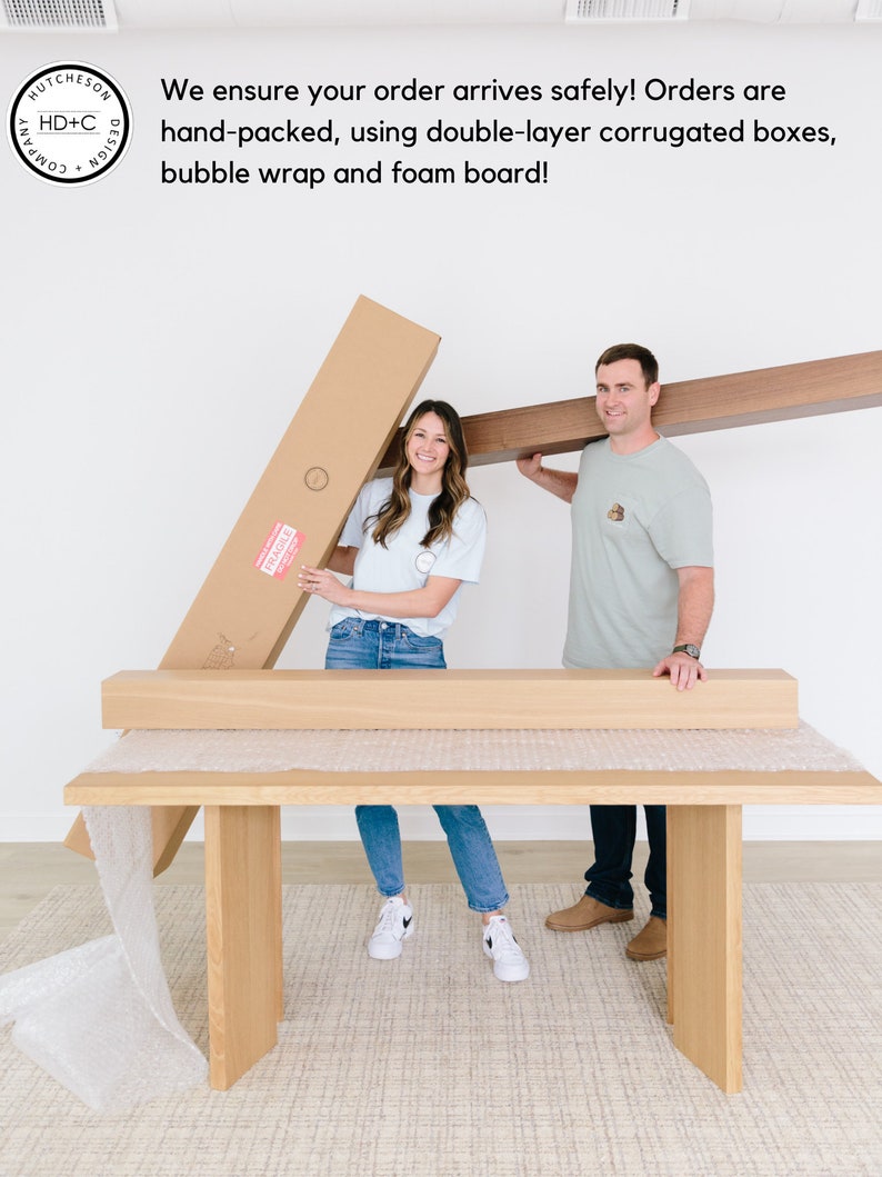 May include: Two people are packing a large wooden table for shipping. The table is wrapped in bubble wrap and secured with cardboard boxes. The text on the box reads "FRAGILE".