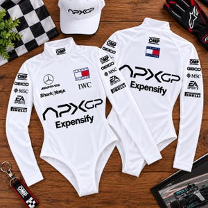 Puede incluir: Dos bodys blancos de manga larga con cuello alto que presentan logotipos negros de APXGP y Expensify, junto con varios logotipos de patrocinadores como Tommy Hilfiger, Mercedes-AMG, OMP, GEICO, MSC, EA Sports y Pirelli, sobre una superficie de madera.