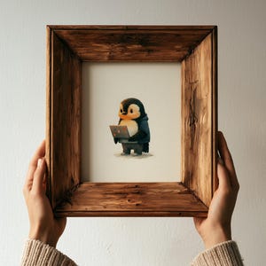 May include: A framed illustration of a small, round penguin standing upright and holding a laptop. The penguin has black and white feathers and is wearing a dark blue hooded garment. The frame is made of dark, textured wood with a rustic finish.