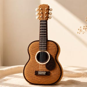 May include: A handcrafted crochet guitar featuring a tan body with dark brown trim, a dark brown fretboard with white stitched frets, and a dark brown pickguard. The headstock includes six white tuning pegs and white strings running down the neck.