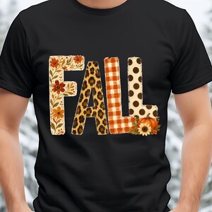 Op de afbeelding: Een zwart T-shirt met korte mouwen en het woord FALL in grote letters. Elke letter heeft een eigen patroon: de F heeft een bloemenprint, de A een luipaardprint, de L een rood-wit ruitpatroon en de L bruine stippen.