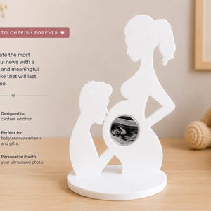 Op de afbeelding: Een wit silhouetbeeld van een zwanger persoon en een partner die voorover leunt, met een ronde uitsparing in de buikstreek voor een echofoto. Het beeld staat op een ronde voet en bevat de tekst: A MEMORY TO CHERISH FOREVER.