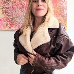 May include: A brown leather jacket with a faux fur collar. The jacket has a zipper closure and multiple pockets.