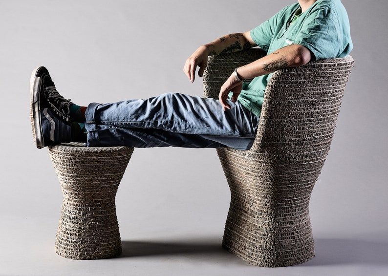 K&ouml;nnte beinhalten: Eine Person sitzt auf einem braunen, geflochtenen Stuhl mit einem passenden Fu&szlig;hocker. Stuhl und Fu&szlig;hocker sind aus recyceltem Karton gefertigt.