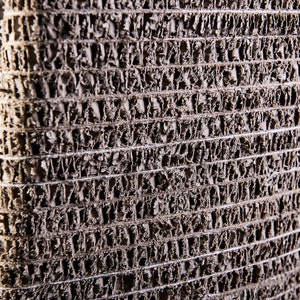K&ouml;nnte beinhalten: Nahaufnahme eines strukturierten, grauen, gewebten Materials mit einem Muster aus kleinen L&ouml;chern. Das Material besteht aus recyceltem Papier und wird zur Herstellung von M&ouml;beln und anderen Gegenst&auml;nden verwendet.