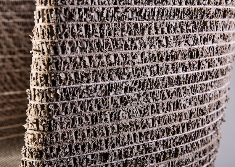 K&ouml;nnte beinhalten: Nahaufnahme eines strukturierten, grauen, gewebten Materials mit einem Muster aus kleinen L&ouml;chern. Das Material besteht aus recyceltem Papier und wird zur Herstellung von M&ouml;beln und anderen Gegenst&auml;nden verwendet.