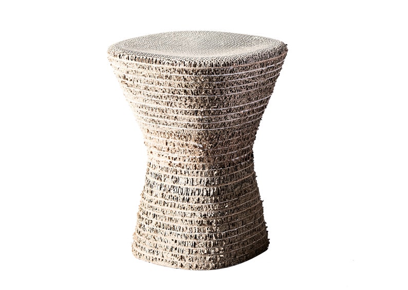 K&ouml;nnte beinhalten: Ein wei&szlig;er Hocker aus Pappe mit einem einzigartigen, strukturierten Design. Der Hocker ist sanduhrf&ouml;rmig und hat eine runde Oberseite.