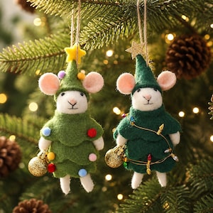 May include: Two felt mouse ornaments hanging by twine. The left mouse wears a light green tree costume with colorful pom-poms and a yellow star. The right mouse wears a dark green tree costume with a string of lights and a gold glitter star.