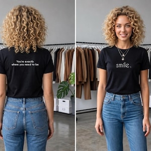 May include: A black short-sleeve t-shirt featuring the word smile. printed in white on the front and the text You're exactly where you need to be printed in white on the back, paired with blue denim jeans.