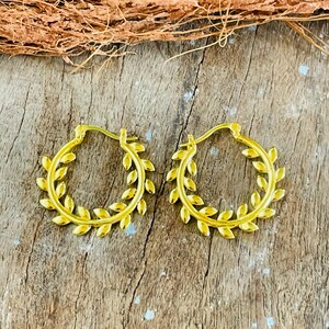May include: A pair of gold hoop earrings featuring a continuous leaf or vine pattern along the outer edge of each circular band. The earrings have a hinged closure mechanism at the top, designed to secure the hoop in place when worn on the ear.