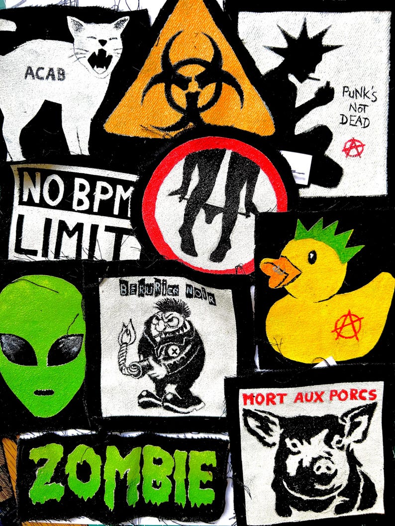 May include: A collection of fabric patches featuring various graphic designs including a white cat with the text ACAB, a yellow biohazard symbol, a silhouette with the text PUNK'S NOT DEAD, a duck with a mohawk, an alien head, and a pig with the text MORT AUX PORCS.