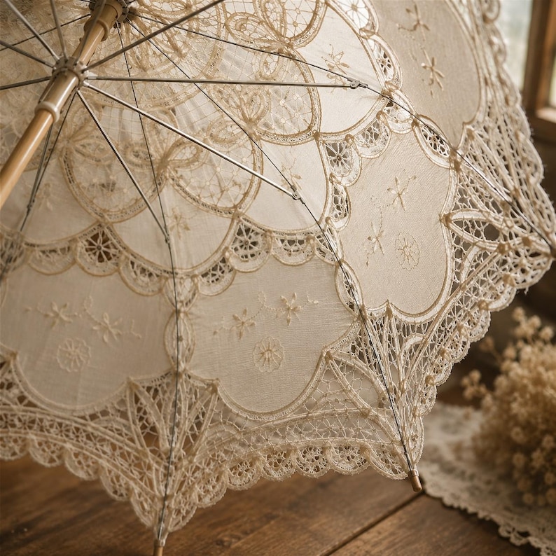 May include: A cream-colored lace parasol featuring intricate floral embroidery and scalloped edges. The canopy is supported by a light-colored wooden handle and thin metal ribs, showcasing detailed needlework patterns throughout the fabric.